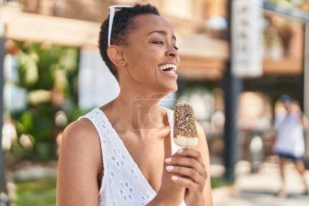 Foto de Mujer afroamericana sonriendo confiada comiendo helado en la calle - Imagen libre de derechos