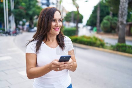 Foto de Joven hermosa mujer hispana sonriendo confiada usando teléfono inteligente en la calle - Imagen libre de derechos