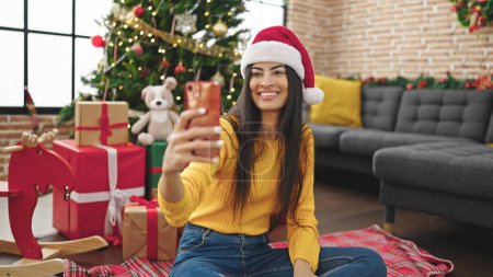Téléchargez les photos : Jeune belle femme hispanique célébrant Noël en prenant des photos selfie par smartphone à la maison - en image libre de droit
