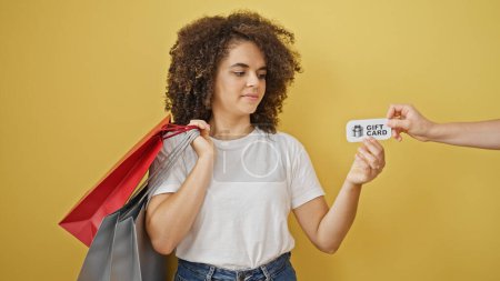Téléchargez les photos : Jeune belle femme hispanique tenant des sacs à provisions recevant une carte cadeau sur fond jaune isolé - en image libre de droit
