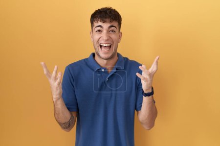 Photo for Young hispanic man standing over yellow background celebrating crazy and amazed for success with arms raised and open eyes screaming excited. winner concept - Royalty Free Image