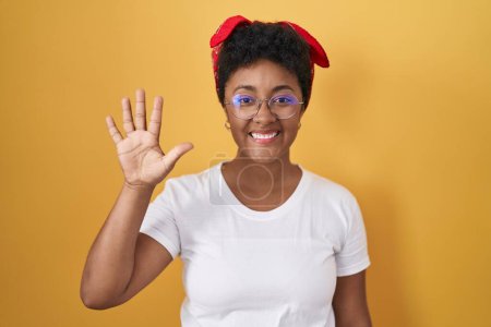 Téléchargez les photos : Jeune femme afro-américaine debout sur fond jaune montrant et pointant vers le haut avec les doigts numéro cinq tout en souriant confiant et heureux. - en image libre de droit