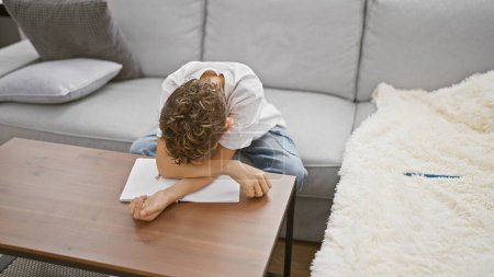 Photo for Adorable blond boy, tired and sleeping, sitting with notebook and book on sofa at home, indoor child leisure with a hint of learning and concentration - Royalty Free Image