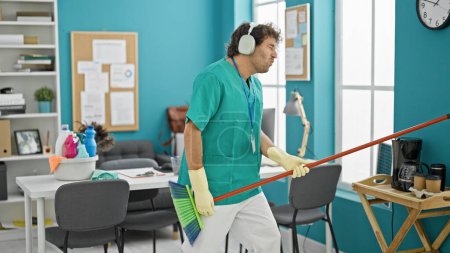 Photo for Young hispanic man professional cleaner playing air guitar dancing at office - Royalty Free Image