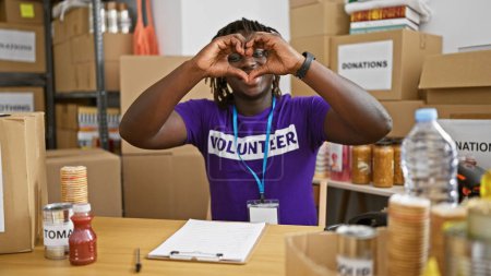 Téléchargez les photos : Afro-américain homme volontaire souriant confiant faire geste de cœur au centre de charité - en image libre de droit