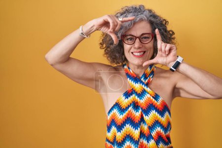 Photo for Middle age woman with grey hair standing over yellow background smiling making frame with hands and fingers with happy face. creativity and photography concept. - Royalty Free Image