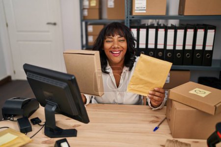 Téléchargez les photos : Hispanique femme travaillant à la petite entreprise commerce électronique tenant des paquets souriant et riant dur à haute voix parce que drôle blague folle. - en image libre de droit