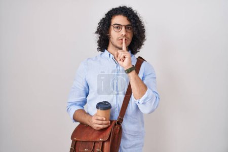 Photo for Hispanic man with curly hair drinking a cup of take away coffee asking to be quiet with finger on lips. silence and secret concept. - Royalty Free Image
