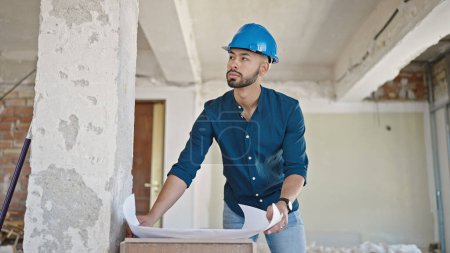 Téléchargez les photos : Jeune architecte hispanique portant un casque dur regardant les plans sur le chantier de construction - en image libre de droit