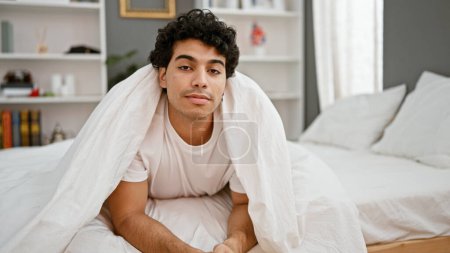 Photo for Young latin man lying on bed covering with bedsheet at bedroom - Royalty Free Image