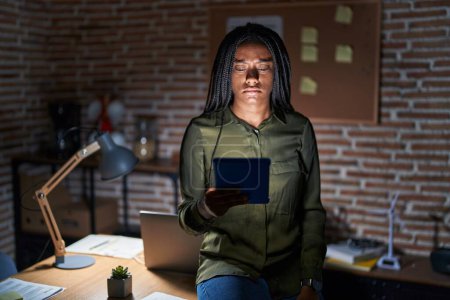 Téléchargez les photos : Jeune afro-américain avec des tresses travaillant au bureau la nuit sceptique et nerveux, fronçant les sourcils contrariés à cause de problèmes. personne négative. - en image libre de droit