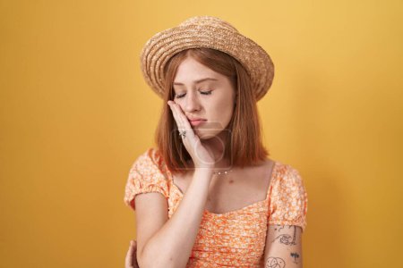 Téléchargez les photos : Jeune rousse femme debout sur fond jaune portant chapeau d'été pensant fatigué et ennuyé avec des problèmes de dépression avec les bras croisés. - en image libre de droit