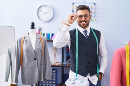 Téléchargez les photos : Jeune homme hispanique tailleur souriant confiance debout au magasin de tailleur - en image libre de droit
