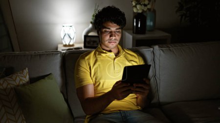Photo for Young latin man using touchpad sitting on sofa at home - Royalty Free Image
