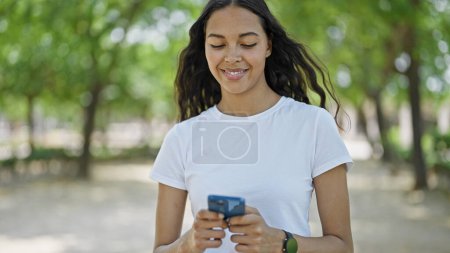 Téléchargez les photos : Femme afro-américaine en utilisant smartphone marche au parc - en image libre de droit