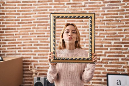 Photo for Hispanic woman holding empty frame looking at the camera blowing a kiss being lovely and sexy. love expression. - Royalty Free Image