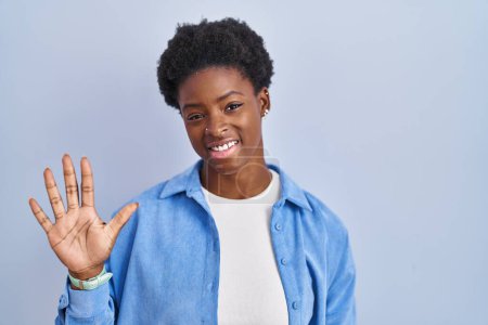 Téléchargez les photos : Femme afro-américaine debout sur fond bleu montrant et pointant vers le haut avec les doigts numéro cinq tout en souriant confiant et heureux. - en image libre de droit