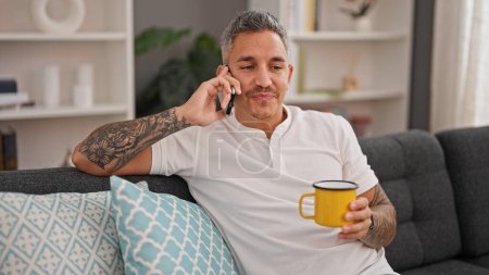 Téléchargez les photos : Jeune homme hispanique parlant sur smartphone boire du café à la maison - en image libre de droit