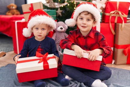 Téléchargez les photos : Adorable garçon et fille souriant confiant tenant cadeau de Noël à la maison - en image libre de droit