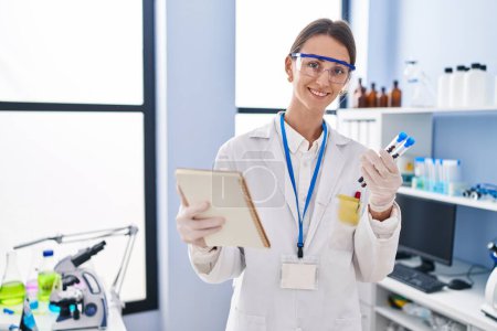Téléchargez les photos : Young caucasian woman scientist holding test tubes reading notebook at laboratory - en image libre de droit