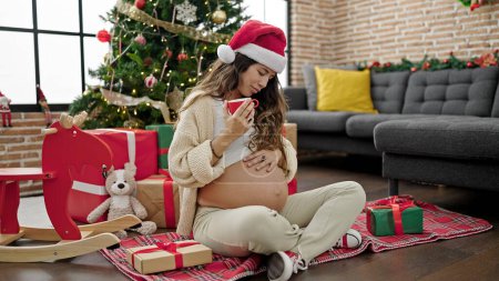 Foto de Joven embarazada bebiendo café celebrando la Navidad en casa - Imagen libre de derechos