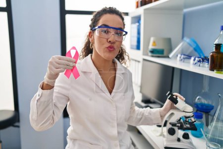 Foto de Mujer hispana joven que trabaja en el laboratorio científico buscando cura para el cáncer de mama mirando a la cámara soplando un beso siendo encantadora y sexy. expresión de amor. - Imagen libre de derechos