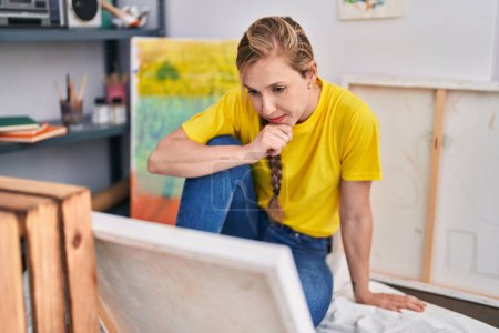 Téléchargez les photos : Jeune artiste blonde regardant dessiner avec une expression sérieuse au studio d'art - en image libre de droit