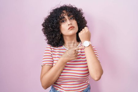 Téléchargez les photos : Jeune femme du Moyen-Orient debout sur fond rose pressé pointant vers regarder le temps, l'impatience, regardant la caméra avec une expression détendue - en image libre de droit