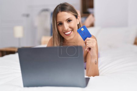 Téléchargez les photos : Young beautiful hispanic woman using laptop and credit card lying on bed at bedroom - en image libre de droit