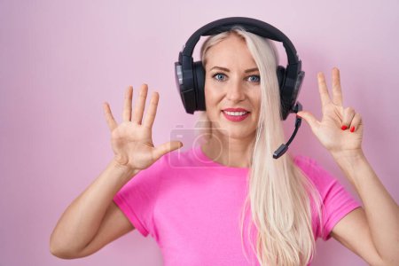 Téléchargez les photos : Femme caucasienne écoutant de la musique à l'aide d'écouteurs montrant et pointant vers le haut avec les doigts numéro huit tout en souriant confiant et heureux. - en image libre de droit