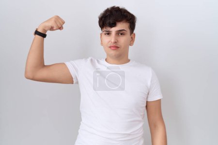 Téléchargez les photos : Jeune homme non binaire portant un t-shirt blanc décontracté personne forte montrant muscle du bras, confiant et fier de la puissance - en image libre de droit