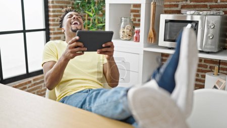 Foto de Hombre afroamericano viendo video en touchpad riendo mucho en el comedor - Imagen libre de derechos
