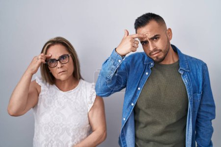 Photo for Hispanic mother and son standing together pointing unhappy to pimple on forehead, ugly infection of blackhead. acne and skin problem - Royalty Free Image
