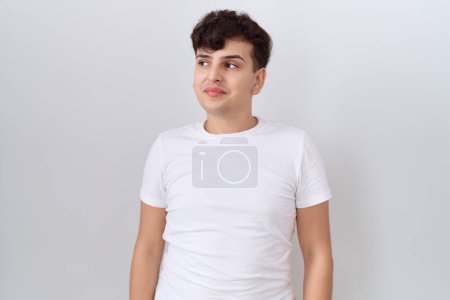 Téléchargez les photos : Jeune homme non binaire portant t-shirt blanc décontracté souriant regardant vers le côté et regardant loin en pensant. - en image libre de droit