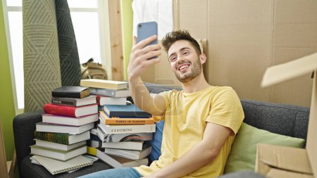 Téléchargez les photos : Jeune homme hispanique prenant des photos selfie avec smartphone assis sur le canapé à la nouvelle maison - en image libre de droit