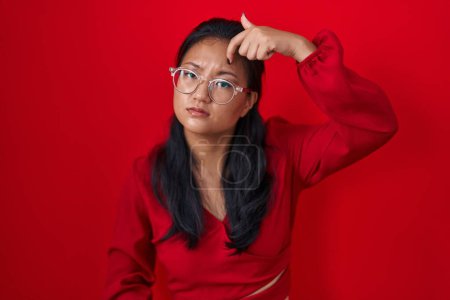 Téléchargez les photos : Asiatique jeune femme debout sur fond rouge pointant malheureux de boutons sur le front, infection laide de la tête noire. acné et problème de peau - en image libre de droit