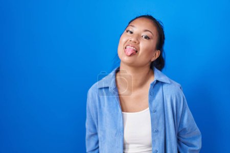 Photo for Asian young woman standing over blue background sticking tongue out happy with funny expression. emotion concept. - Royalty Free Image