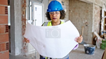 Photo for Young beautiful latin woman builder looking house project at construction site - Royalty Free Image