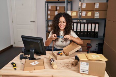 Foto de Joven mujer hispana hermosa comercio electrónico trabajador de negocios hacer foto al paquete de pulsera en la oficina - Imagen libre de derechos