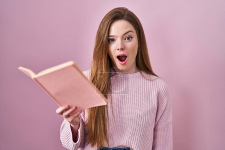 Photo for Young caucasian woman reading a book over pink background afraid and shocked with surprise and amazed expression, fear and excited face. - Royalty Free Image