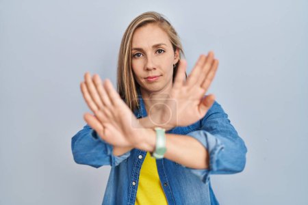 Photo for Young blonde woman standing over blue background rejection expression crossing arms and palms doing negative sign, angry face - Royalty Free Image