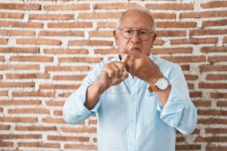 Téléchargez les photos : Homme âgé avec les cheveux gris debout au-dessus des briques expression de rejet de mur en croisant les doigts faisant signe négatif - en image libre de droit