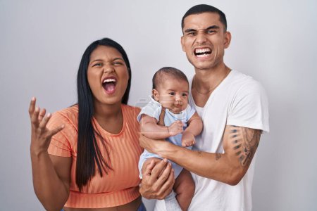 Photo for Young hispanic couple with baby standing together over isolated background crazy and mad shouting and yelling with aggressive expression and arms raised. frustration concept. - Royalty Free Image