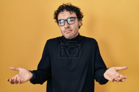 Photo for Hispanic man standing over yellow background clueless and confused with open arms, no idea concept. - Royalty Free Image