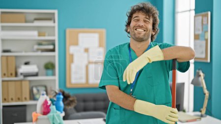 Photo for Young hispanic man professional cleaner holding mop smiling at office - Royalty Free Image
