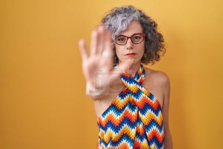 Photo for Middle age woman with grey hair standing over yellow background doing stop sing with palm of the hand. warning expression with negative and serious gesture on the face. - Royalty Free Image