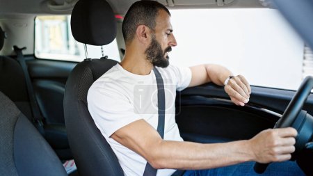 Photo for Young hispanic man driving car looking watch at street - Royalty Free Image
