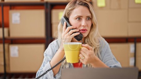 Téléchargez les photos : Jeune femme blonde ecommerce travailleur d'affaires parlant au téléphone boire du café au bureau - en image libre de droit