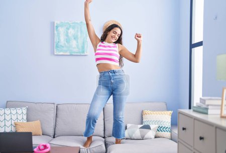 Téléchargez les photos : Jeune belle femme hispanique souriante danse confiante sur le canapé à la maison - en image libre de droit