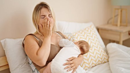 Photo for Mother and daughter sitting on bed breastfeeding baby tired yawning at bedroom - Royalty Free Image